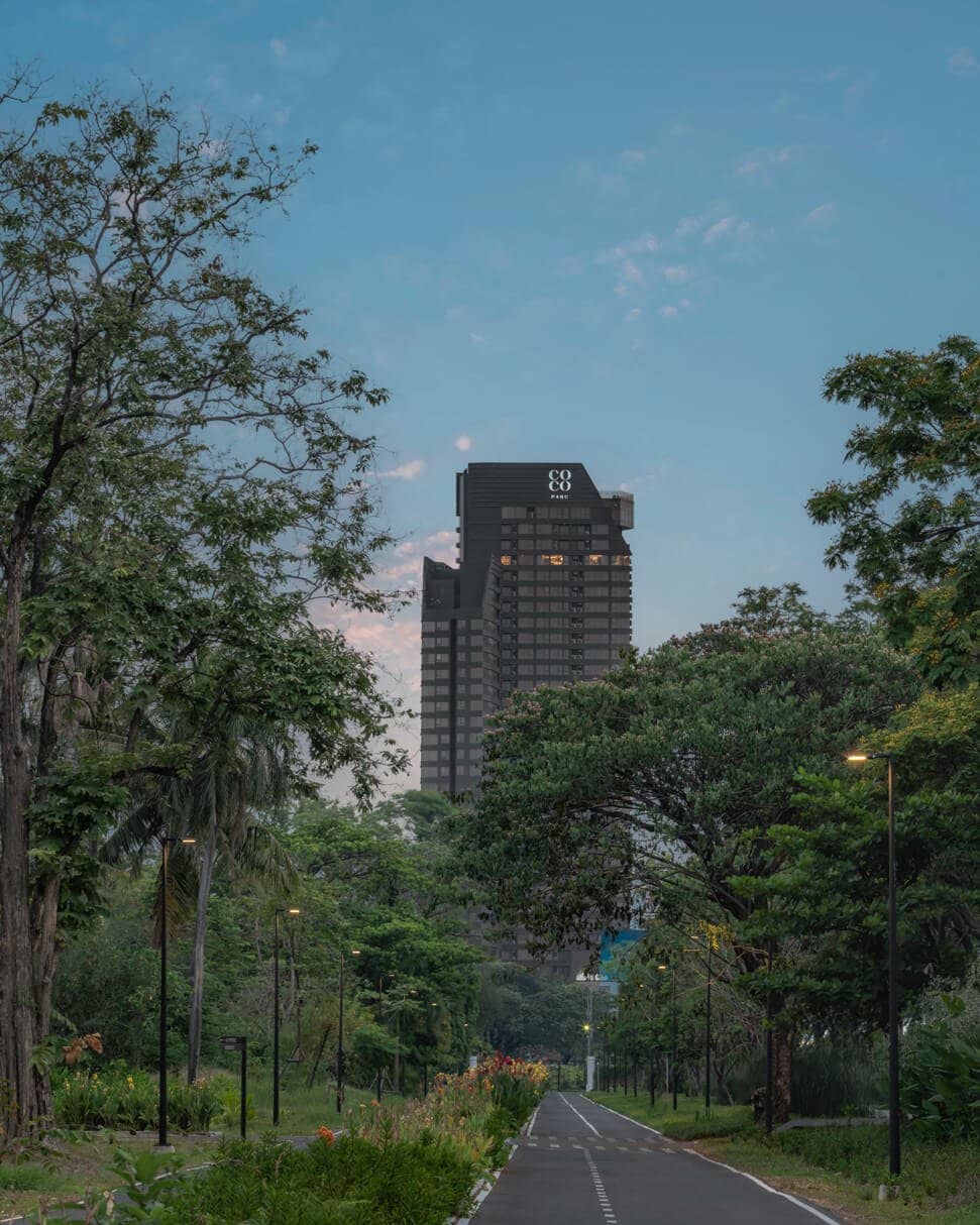COCO Parc tower framed by tall trees along a road