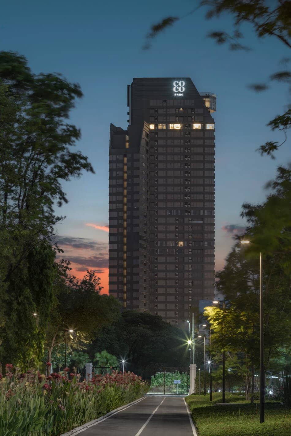 COCO Parc tower lit up at dusk above a tree-lined road
